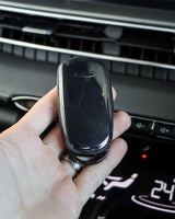 Hand holding a car key fob in front of a car's infotainment screen.