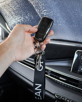 Hand holding a car key fob with a lanyard inside a vehicle.
